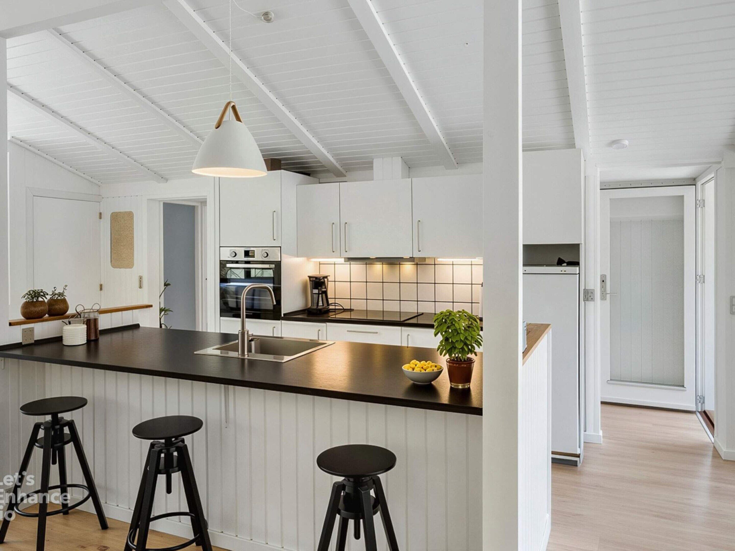 Et moderne køkken med hvide skabe, en sort bordplade og en central ø med barstole.