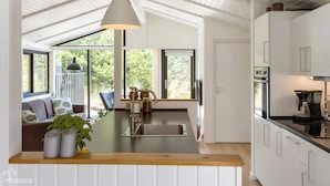 A modern kitchen with a central island, white cabinetry, and a large window providing a view of greenery. - 4 Star Holiday Home in Blokhus (Blokhus)