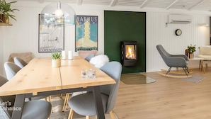 A modern living room with a wooden dining table, grey chairs, a green accent wall, a fireplace, and a wall-mounted clock. - 4 Star Holiday Home in Blokhus (Blokhus)