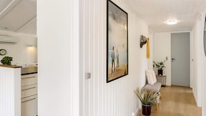 A hallway with white paneled walls, a framed picture, a potted plant, and a door leading to another room. - 4 Star Holiday Home in Blokhus (Blokhus)