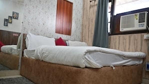 Un dormitorio con un sofá cama marrón, un colchón blanco y una almohada roja. Hay una ventana con un aire acondicionado en la pared.