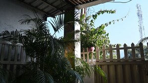 Un espacio al aire libre techado con cercado de madera, plantas en macetas y una vista despejada de una torre de comunicaciones al fondo.