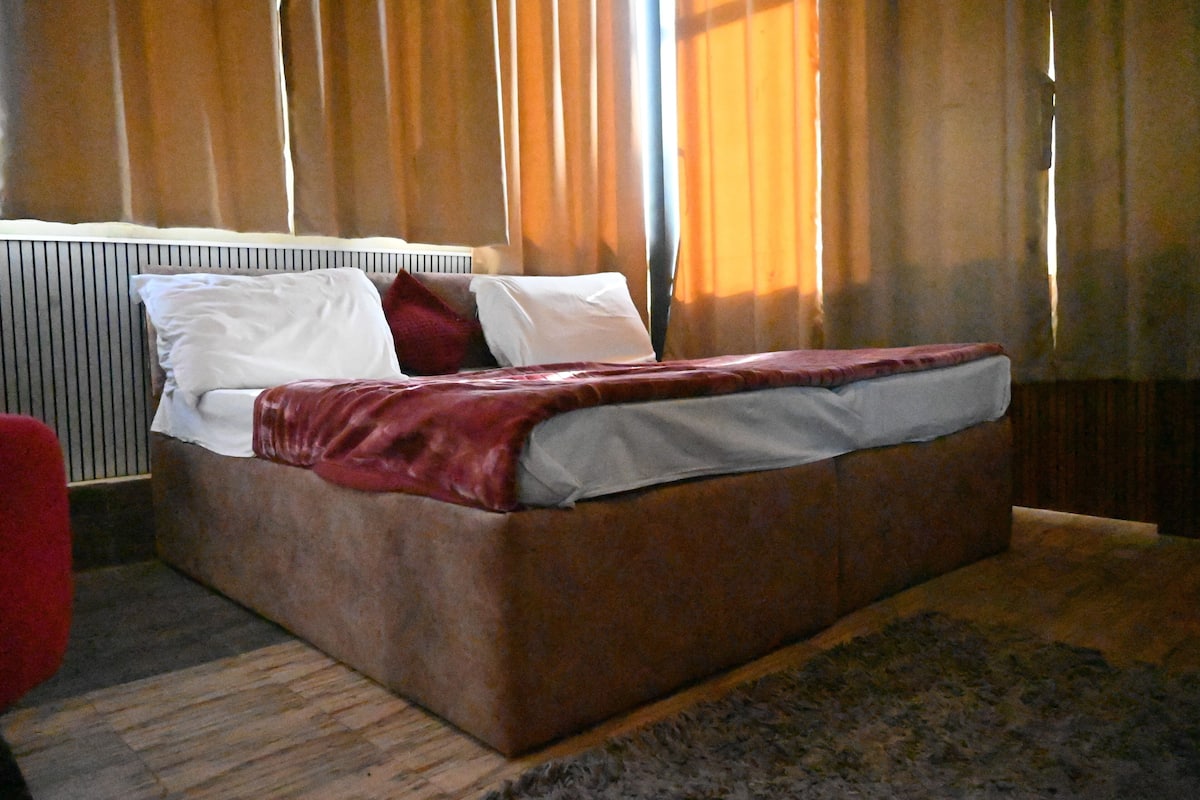 A bed with a red blanket and white pillows, a wooden headboard, and a window with curtains.