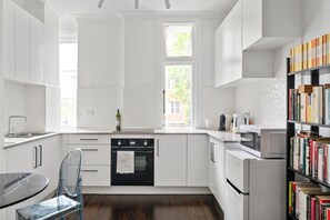 A modern kitchen with white cabinetry, a built-in oven, a microwave, and a bookshelf filled with books. - Prime Apartment in Darlinghurst (Darlinghurst)