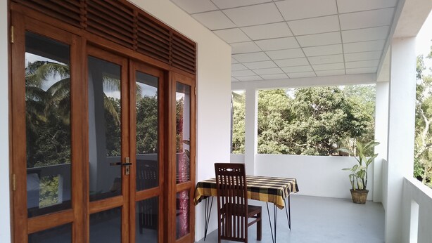 Un balcón con una puerta de madera, una mesa con mantel a cuadros y una silla.