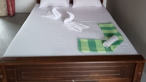Una cama bien hecha con sábanas blancas, cabecera de madera y una toalla verde y blanca a rayas.