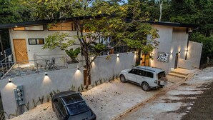 Ett modernt hus i två våningar med en täckt uteplats, en vit SUV parkerad på uppfarten och en svart bil parkerad längre fram.