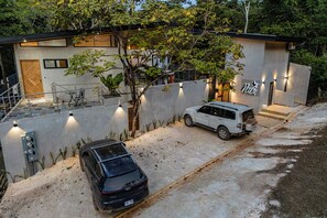 Une maison moderne à deux étages, dotée d’un patio couvert, avec un VUS blanc garé dans l’allée et une voiture noire stationnée au premier plan.