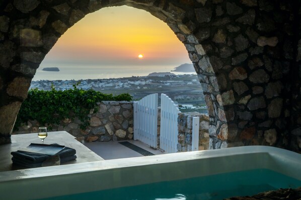 A stone archway leading to a pool with a sunset view.