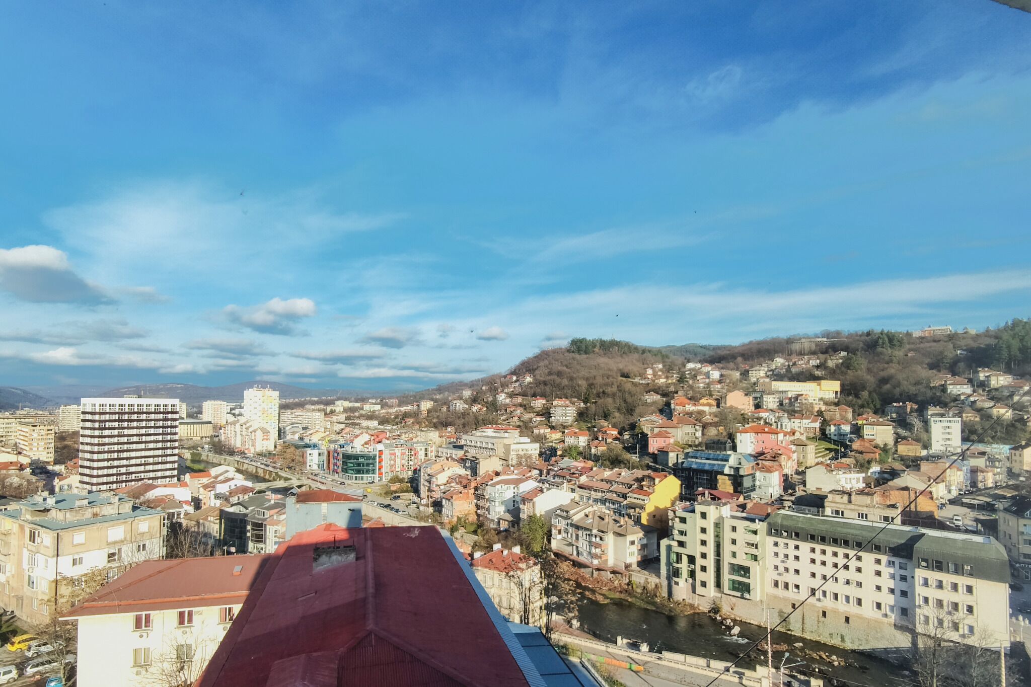A cityscape with a river, buildings, and a hilly background.