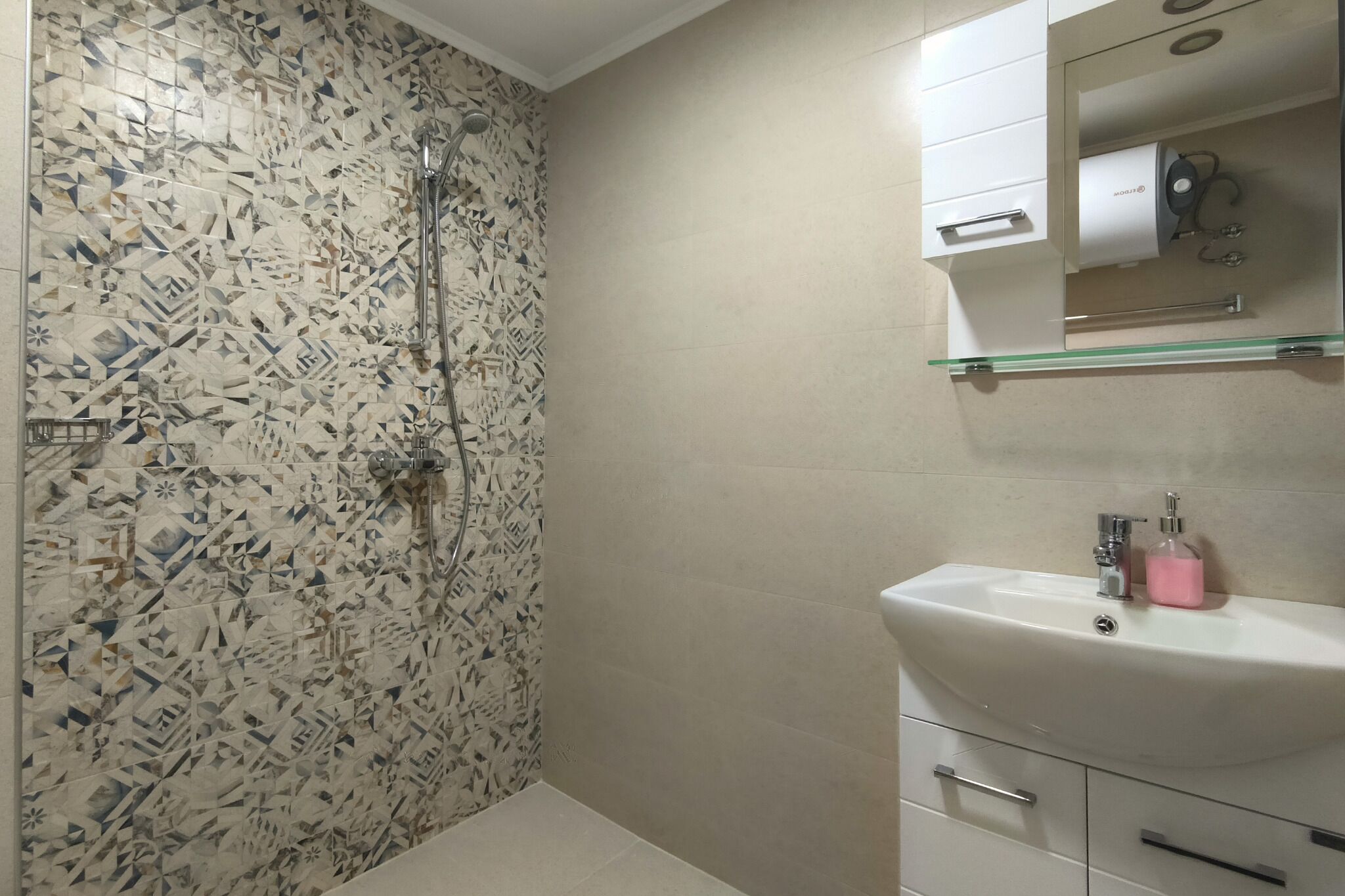 Een badkamer met een douche, een wastafel en een spiegel.