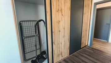 A room with a wooden floor, a metal rack with a vacuum cleaner, and a door with a wooden panel.