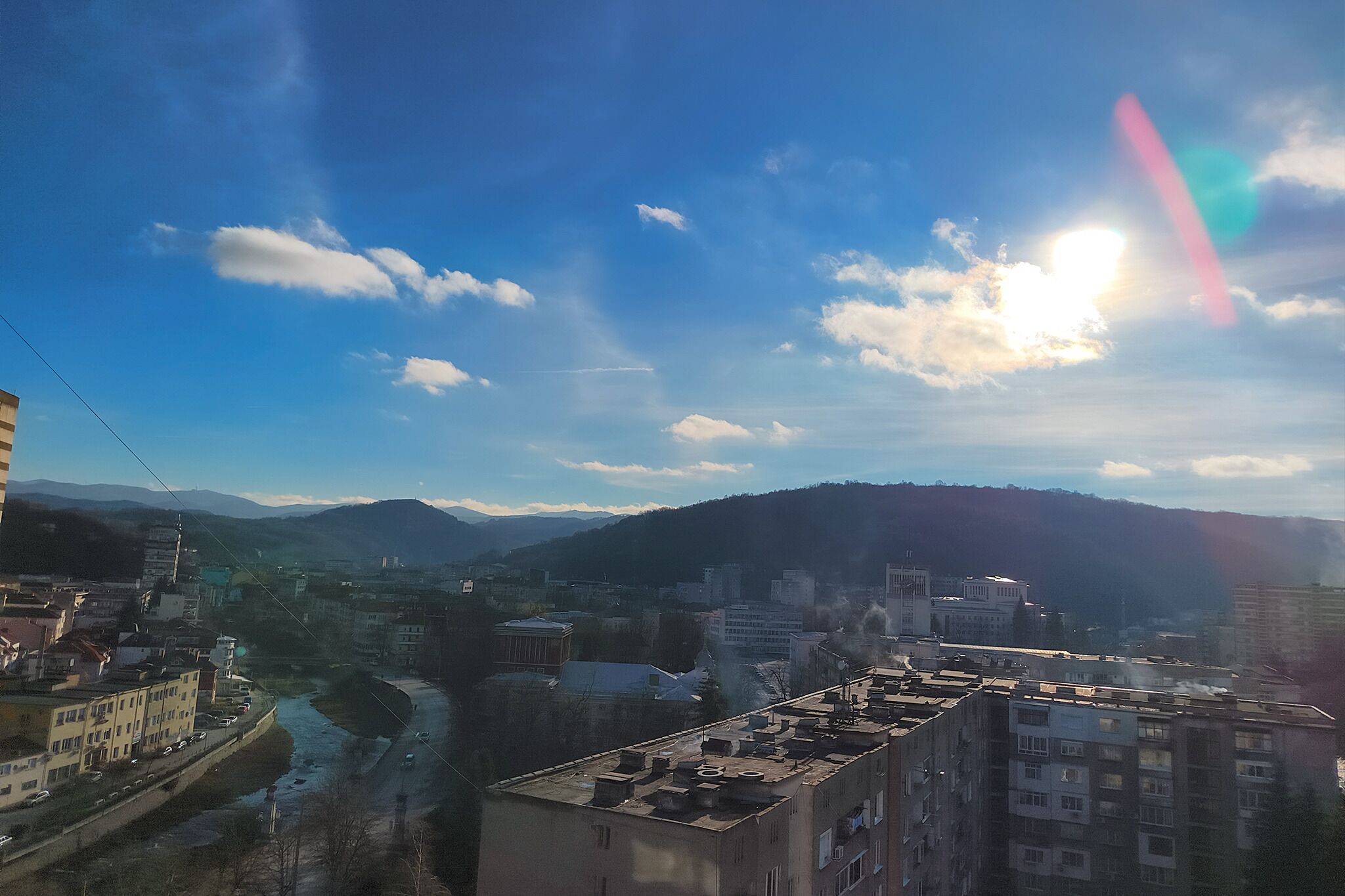 Une vue urbaine avec des bâtiments, une rivière et des montagnes en arrière-plan.