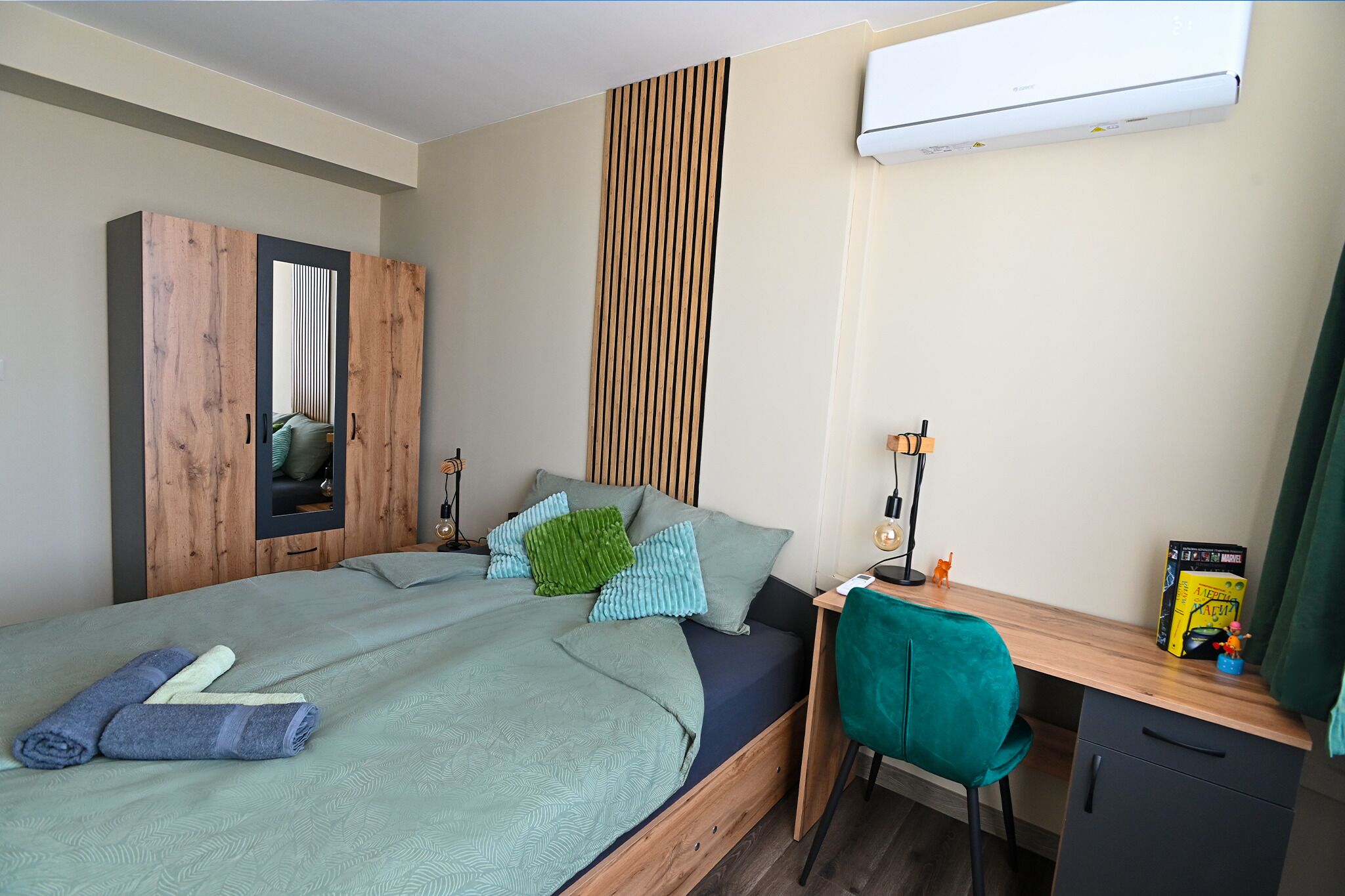 A bedroom with a bed, a desk, a chair, a wardrobe, and an air conditioner.