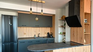 Une cuisine moderne dotée d’un réfrigérateur encastré, de meubles de couleur sombre, d’un plan de travail en bois et de luminaires suspendus.