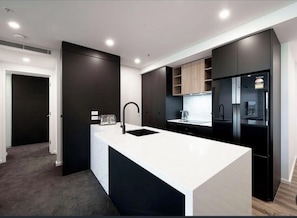 A modern kitchen with a central island, dark cabinetry, and built-in appliances.