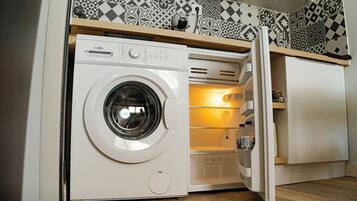 A compact laundry room with a front-loading washing machine, a built-in refrigerator, and a shelf above the washing machine.