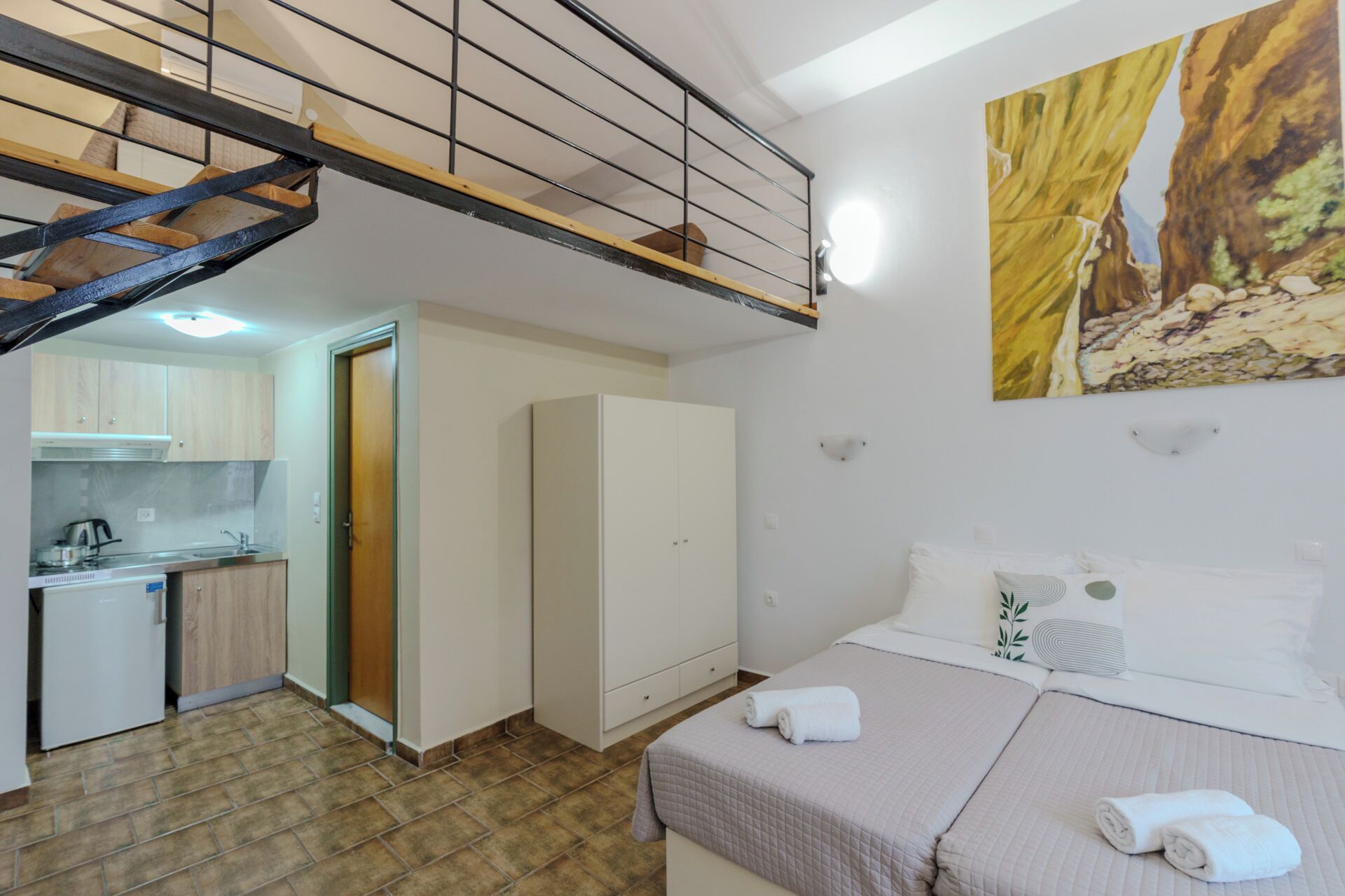 A bedroom with a bed, a painting, and a staircase leading to a kitchen.