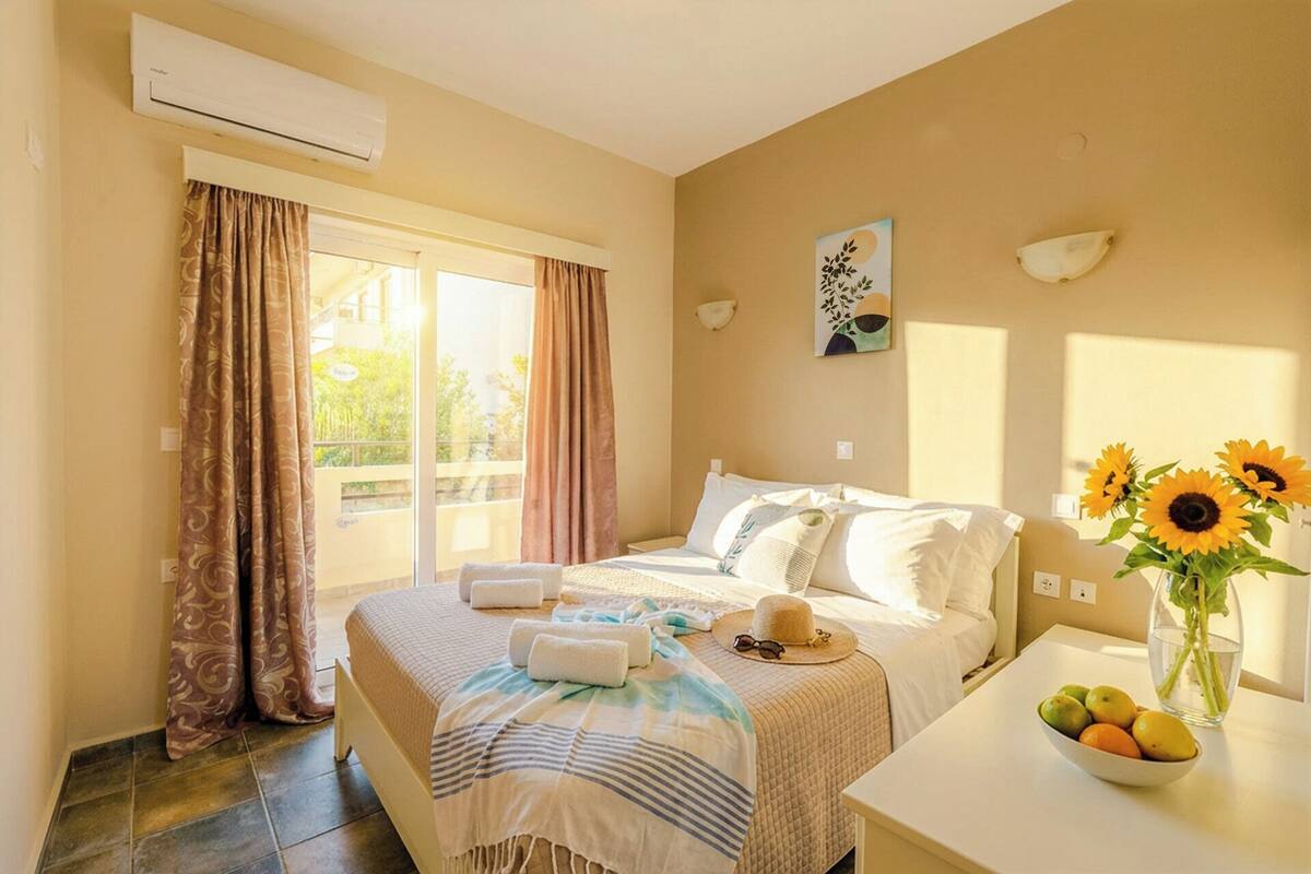 A hotel room with a bed, a desk with a vase of flowers, and a view of greenery outside.