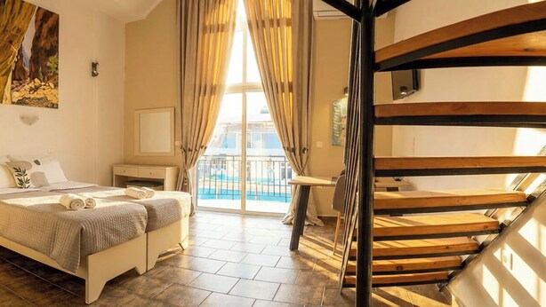 Ein Schlafzimmer mit Bett, Nachttisch, einem Gemälde, einem Fenster mit Vorhängen und einer Holztreppe.