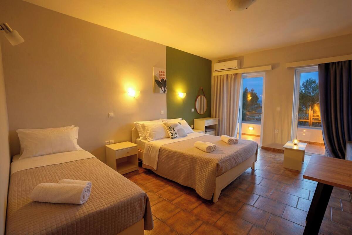 A hotel room with two beds, a small table, and a balcony with curtains.