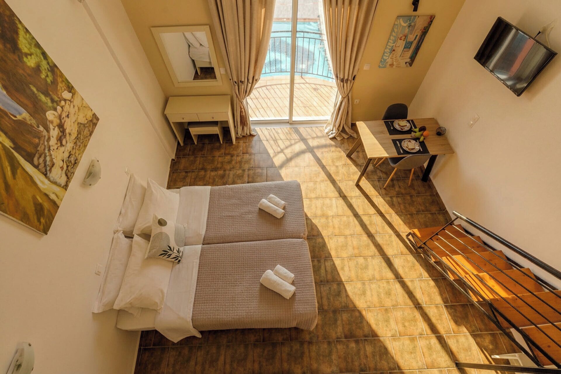 A hotel room with a bed, a desk, a chair, a small table with food, and a window with curtains.