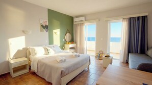 Ein Hotelzimmer mit Bett, Nachttischen, einem Schreibtisch und Blick auf das Meer.
