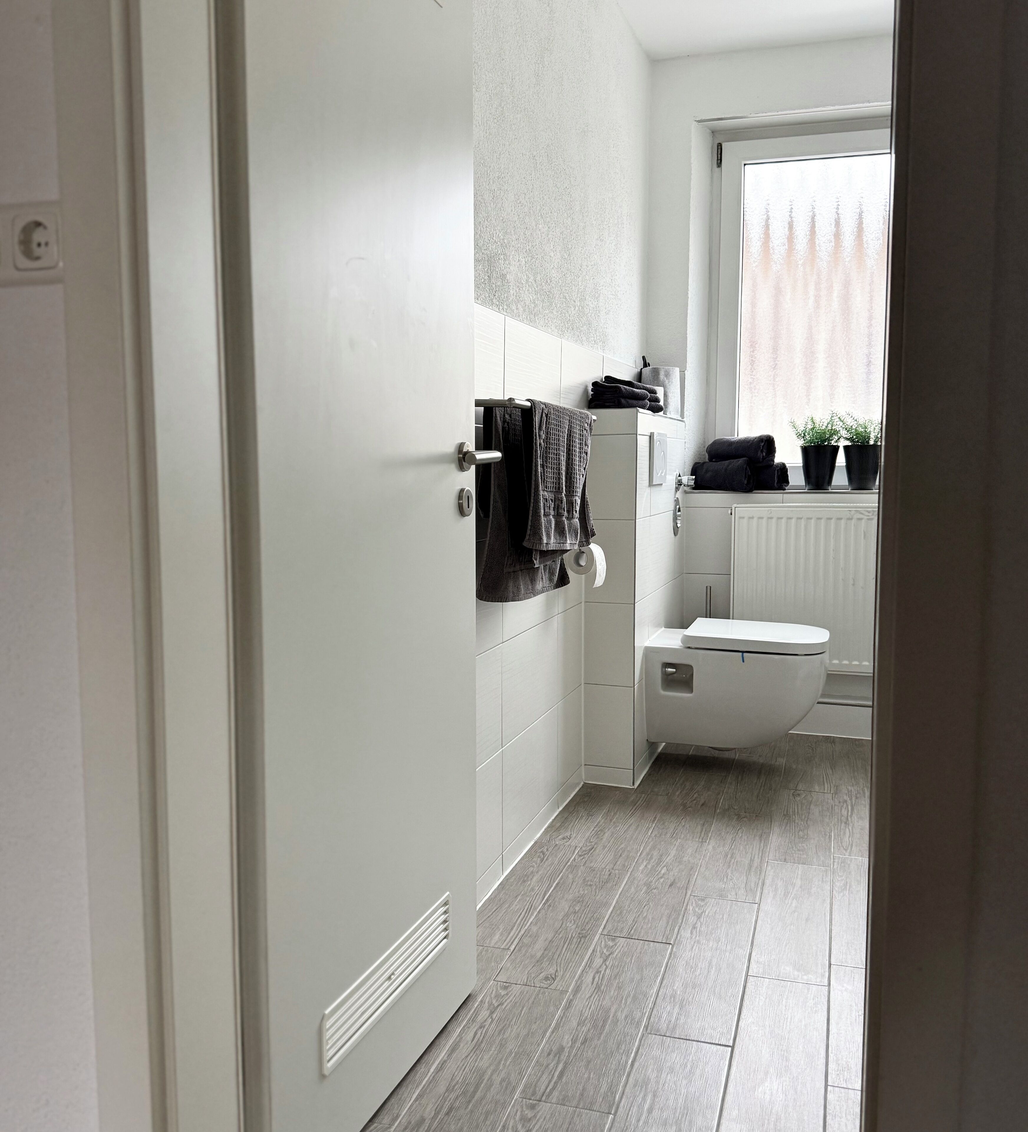 Un bagno moderno con servizi igienici, porta asciugamani e una finestra con piante.