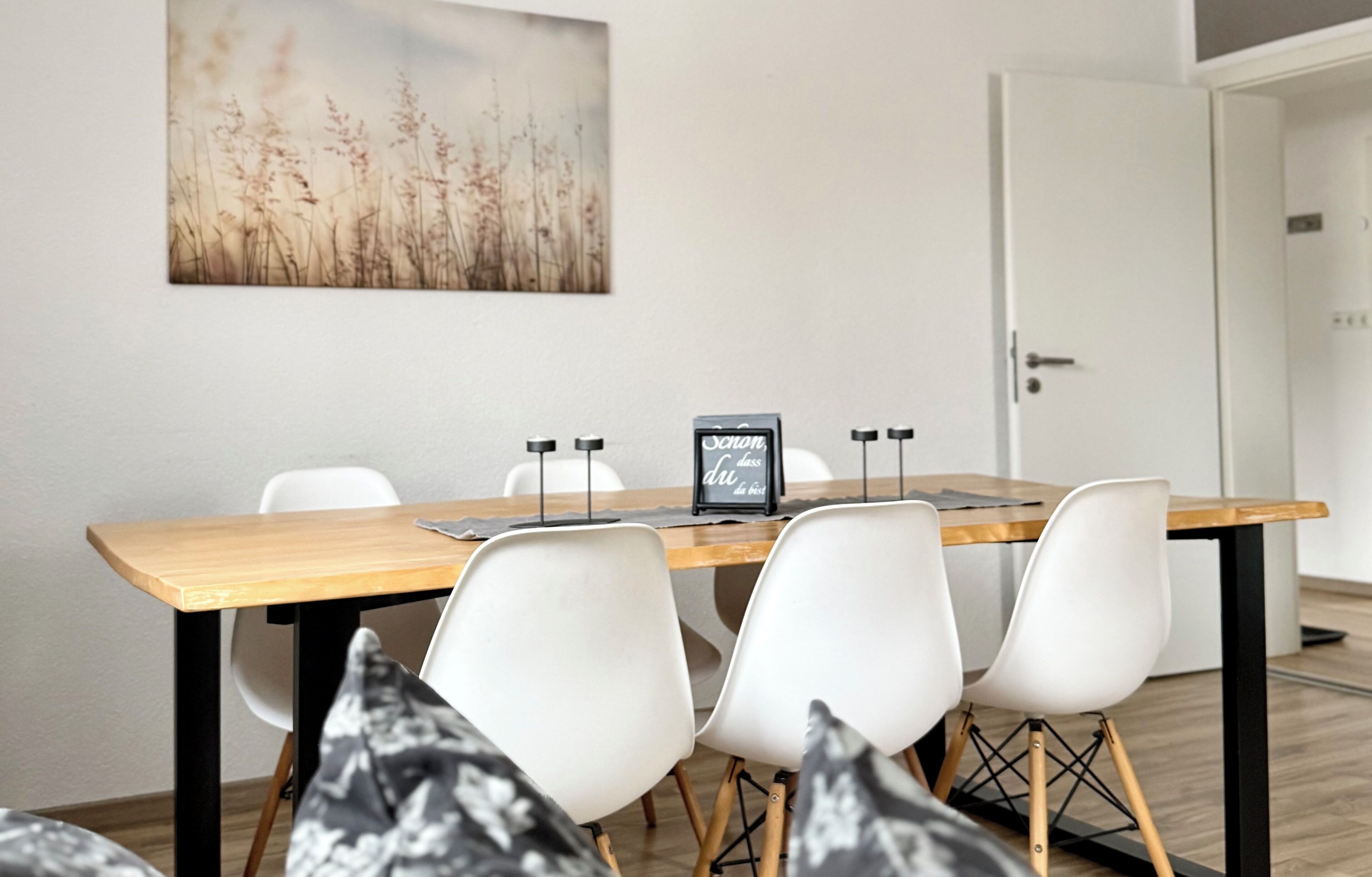 Een eethoek met een houten tafel, witte stoelen en een schilderij aan de muur.