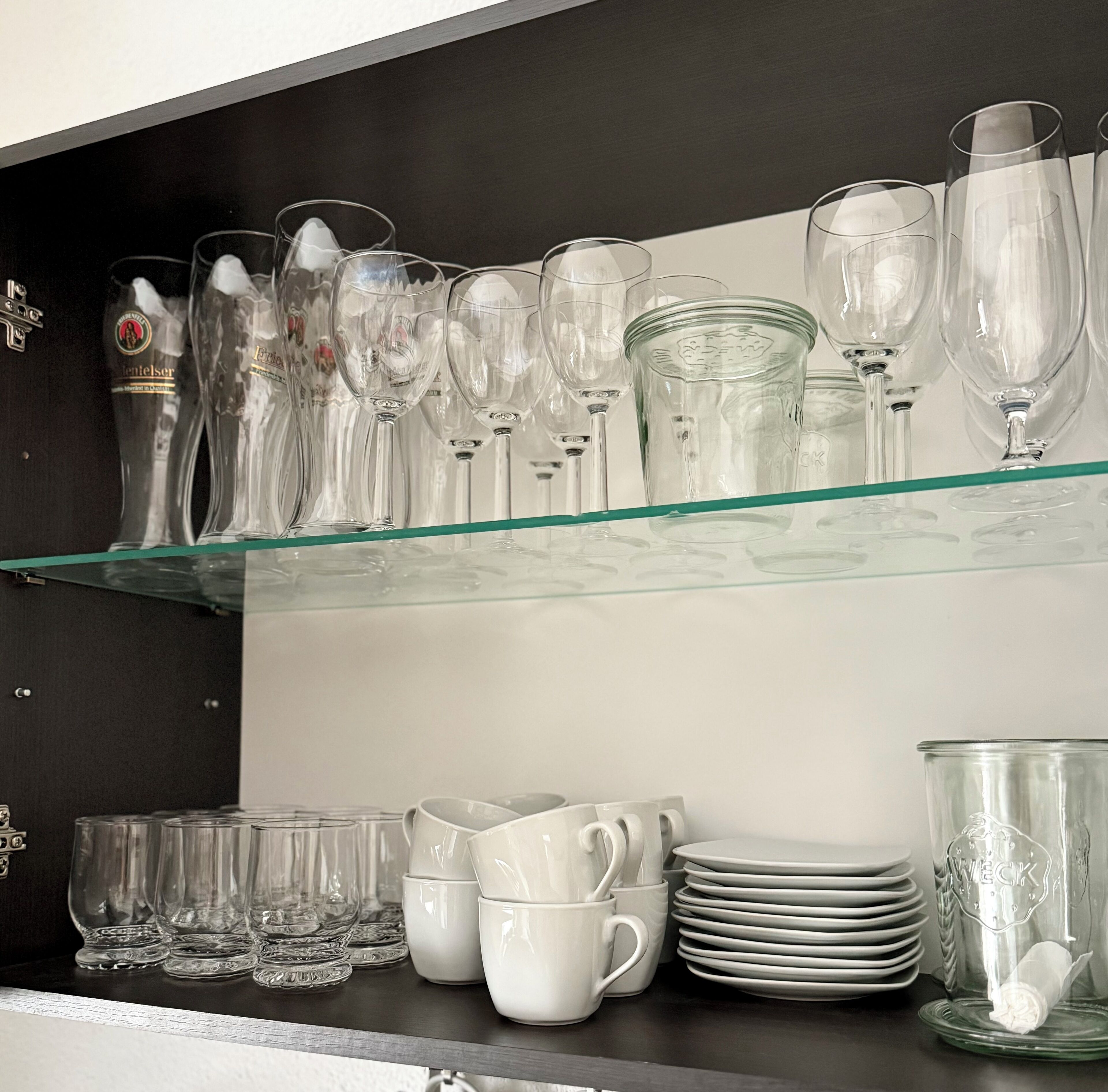 Eine Gläserausstellung mit verschiedenen Glasarten, darunter Weingläser, Trinkgläser und Tassen, angeordnet auf Regalen.