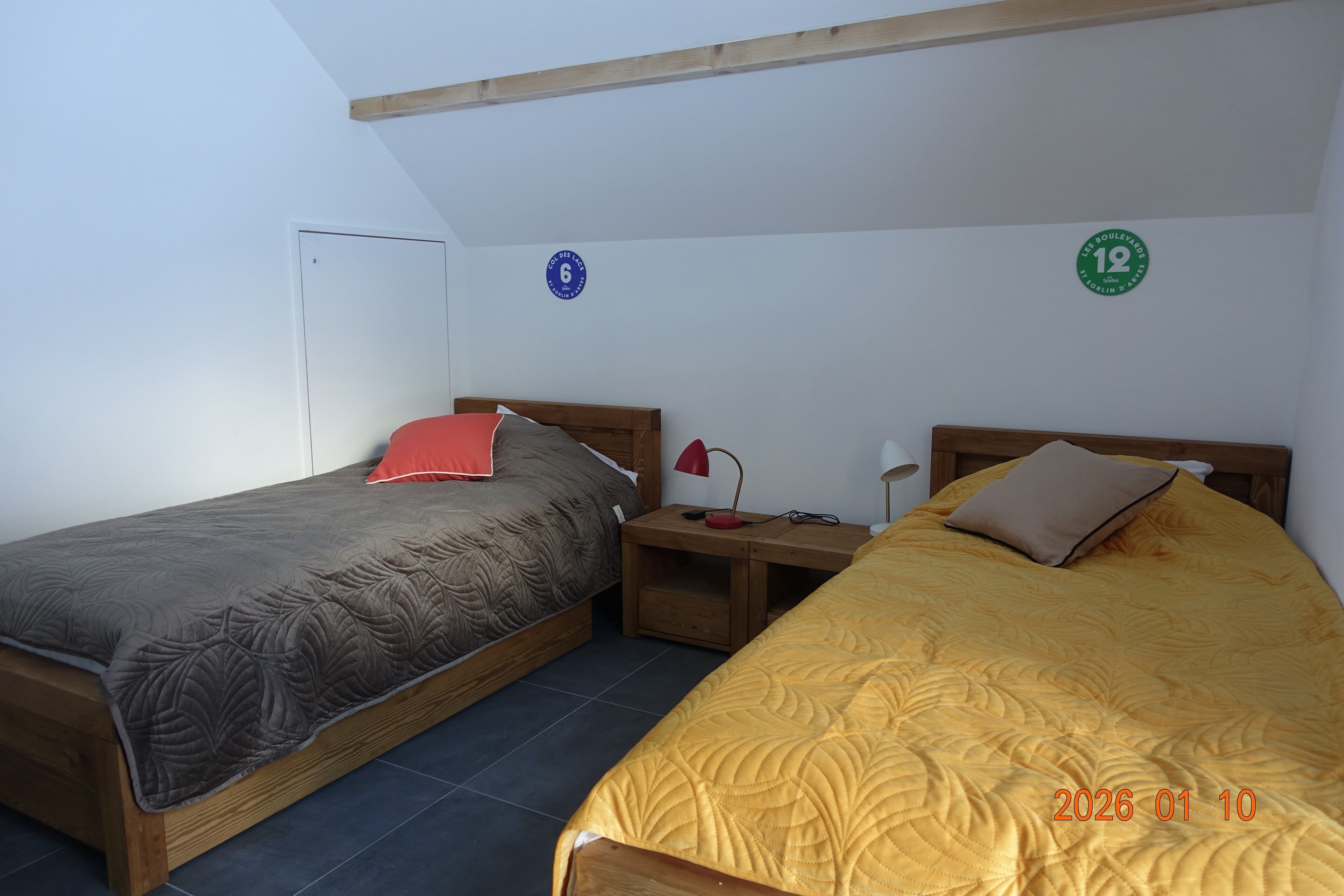 Ein Zimmer mit zwei Betten, jedes mit einer eigenen Tagesdecke, einem Nachttisch mit Lampe und einer Tür.