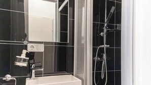 A modern bathroom with a white sink, a handheld showerhead, and a glass-enclosed shower area. - Bright 1BR Apt Perfect for Long Stays (Vienna)