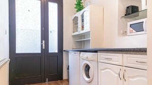 A compact kitchen with a washing machine, white cabinets, and a microwave on the countertop. - Bright 1BR Apt Perfect for Long Stays (Vienna)