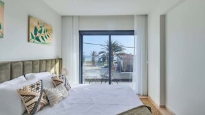Quarto com cama, almofadas, vista para o exterior e obras de arte na parede.