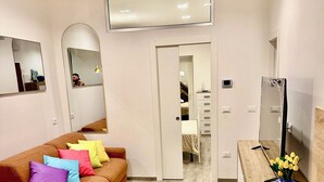 Ein modernes Wohnzimmer mit einem braunen Sofa, bunten Kissen, einem Couchtisch aus Holz und einem Fernseher auf einem Holzschrank.
