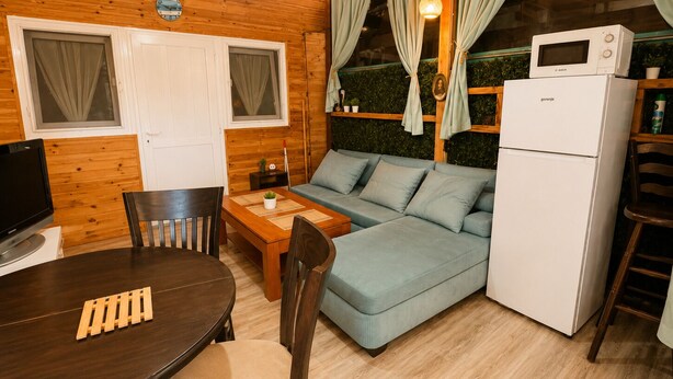 L’intérieur chaleureux d’un chalet, avec un revêtement mural en bois, un canapé, une table à manger, des chaises, un téléviseur et un réfrigérateur.