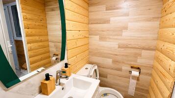 A bathroom with wooden panel walls, a white sink, a toilet, and a mirror.