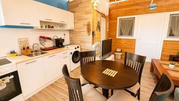 A compact kitchen with a washing machine, a dining table with chairs, and a TV.