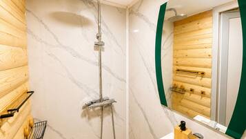A modern bathroom with a shower, a wooden wall panel, a marble-tiled wall, and a mirror with a green frame.