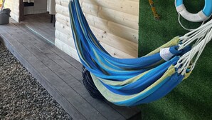 Une terrasse en bois avec un hamac, un mur en bois orné d’une décoration murale tissée et un anneau de sauvetage.