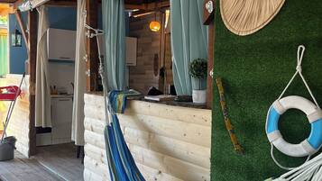 A wooden deck with a hammock, a wooden wall with a woven wall hanging, and a lifebuoy.