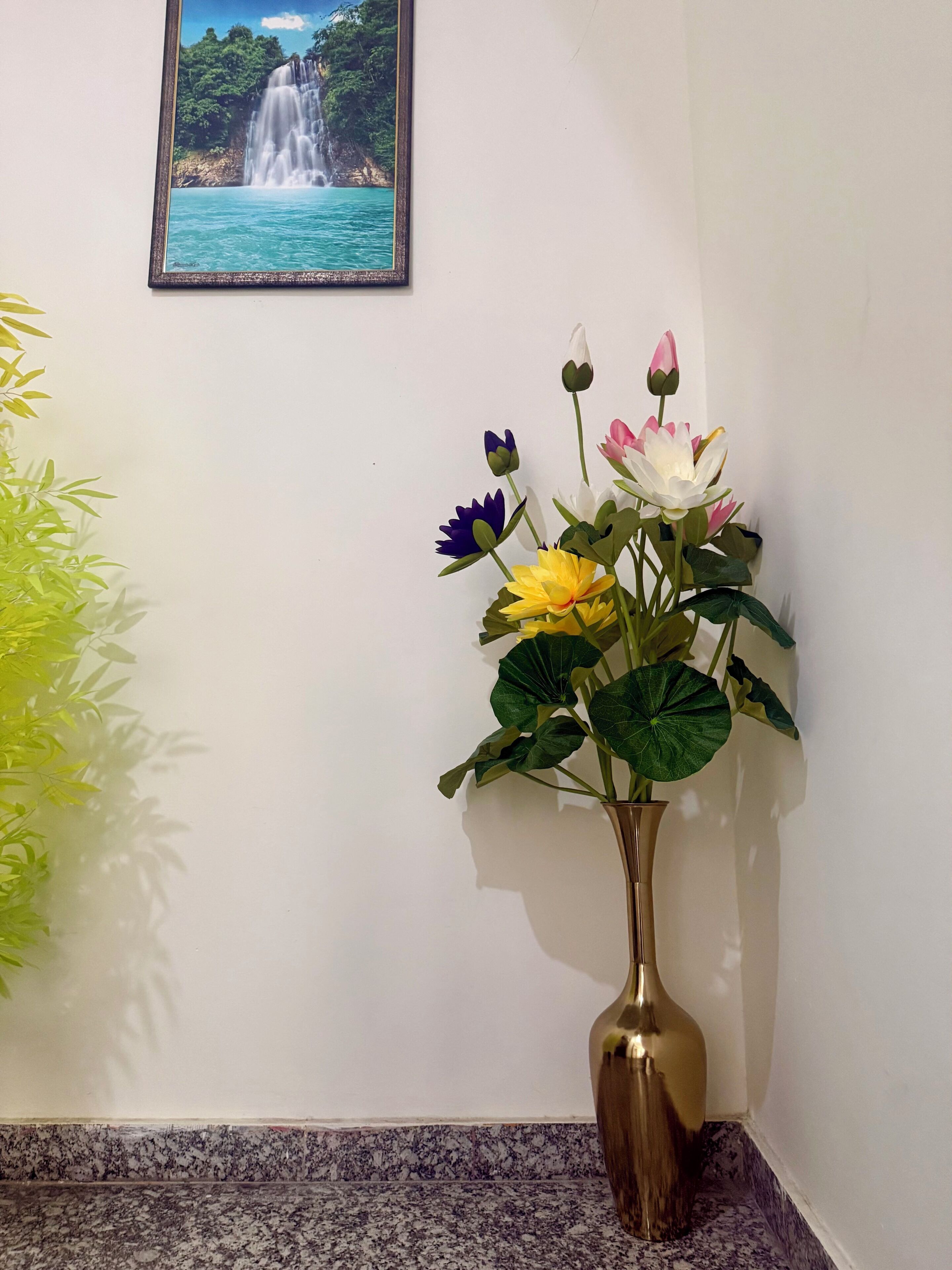 A corner of a room with a marble floor, a wall-mounted picture of a waterfall, and a vase with flowers.
