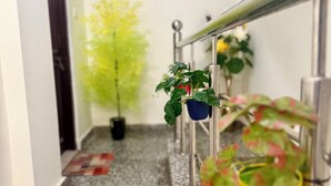 A hallway with a granite floor, potted plants, a metal railing, and a framed picture on the wall. - Saroj Serenity inn (Rishikesh)