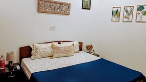 A bedroom with a bed, a nightstand, a lamp, and wall art. - Saroj Serenity inn (Rishikesh)