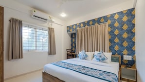 A bedroom with a bed, curtains, a window, an air conditioning unit, and a patterned wall. - Hotel Royal Manyaa (Bengaluru)