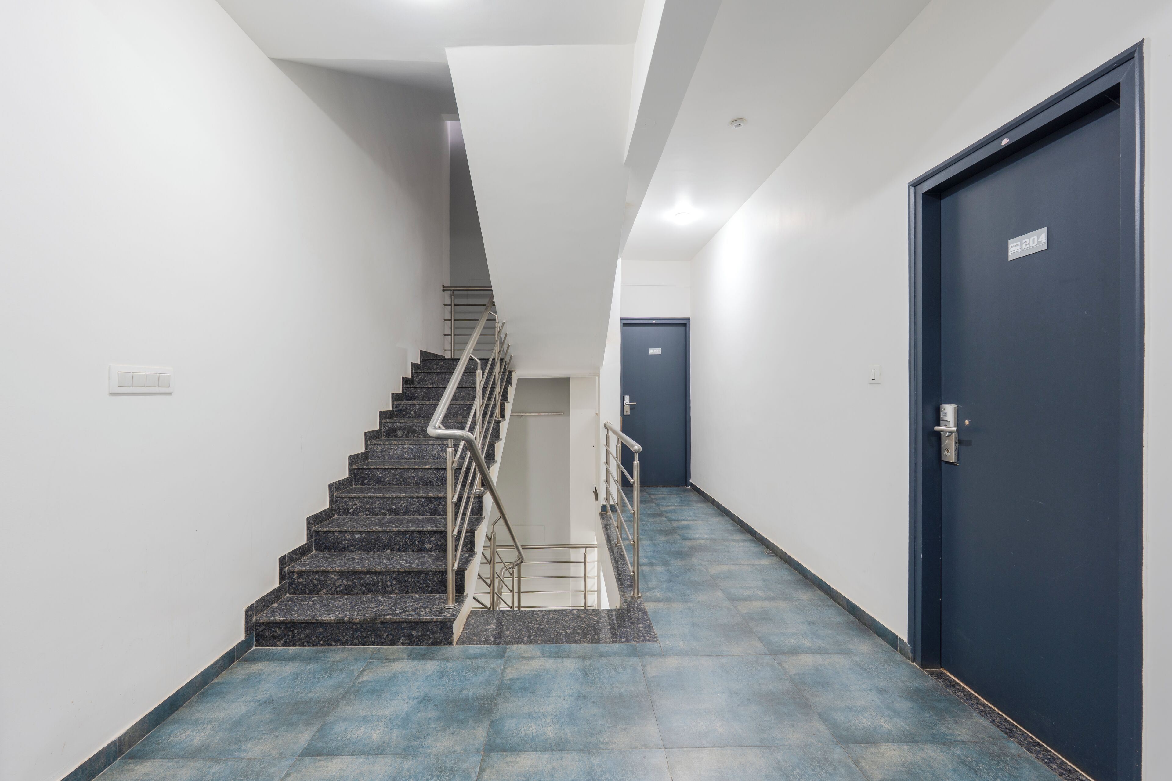 A hallway with a staircase, a blue door, and a white wall.