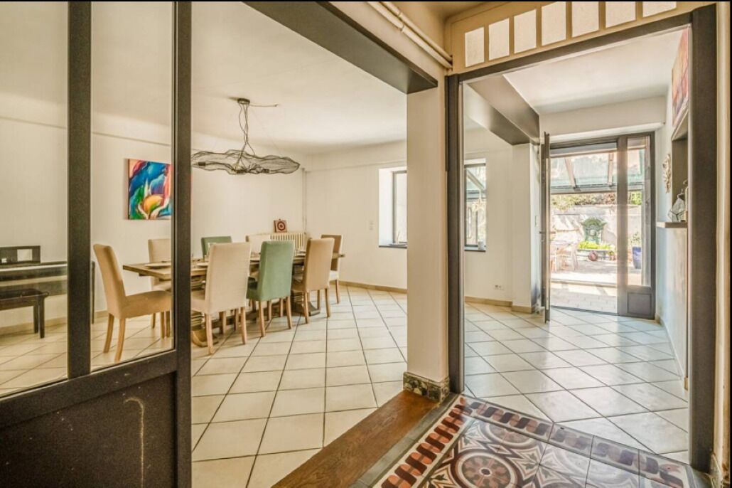 Un vaste espace dédié à la salle à manger, doté d’un sol carrelé, d’une table à manger avec des chaises et d’un tableau coloré accroché au mur.