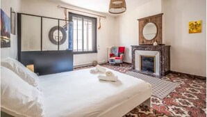 Quarto com cama, cadeira, lareira e um espelho grande.