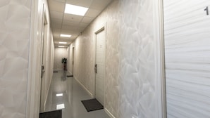 Um corredor com paredes estampadas com padrão geométrico, uma porta com o número 1 e uma planta em vaso ao fundo.