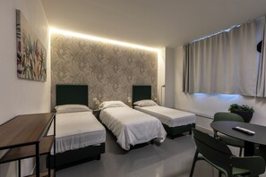 A hotel room with two single beds, a small desk, a chair, a table, and a potted plant. - SMART ROOMS Foresteria (Viadana)